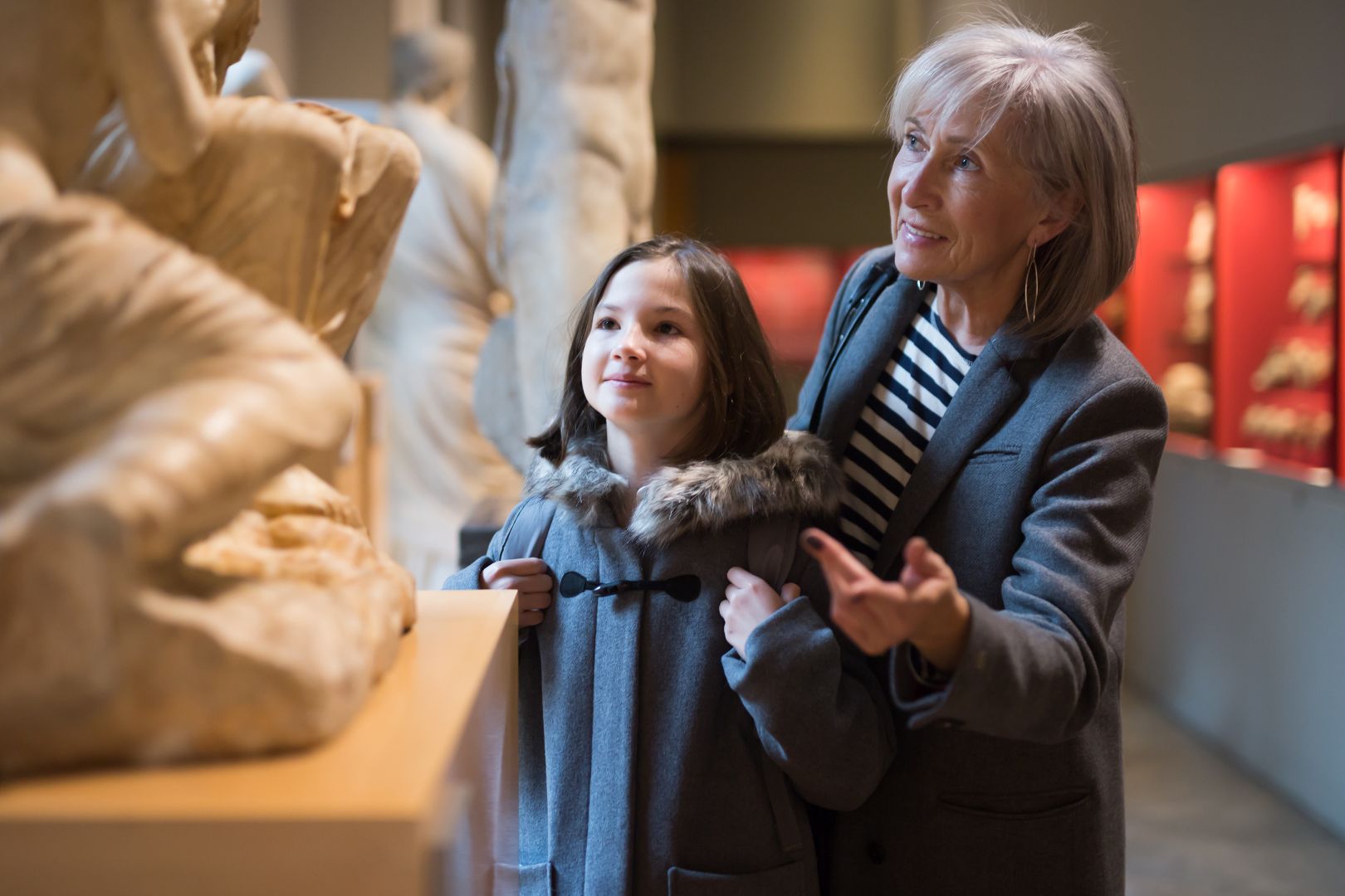 A grandmother and her granddaughter explore a museum exhibit together. They are looking at art sculptures.