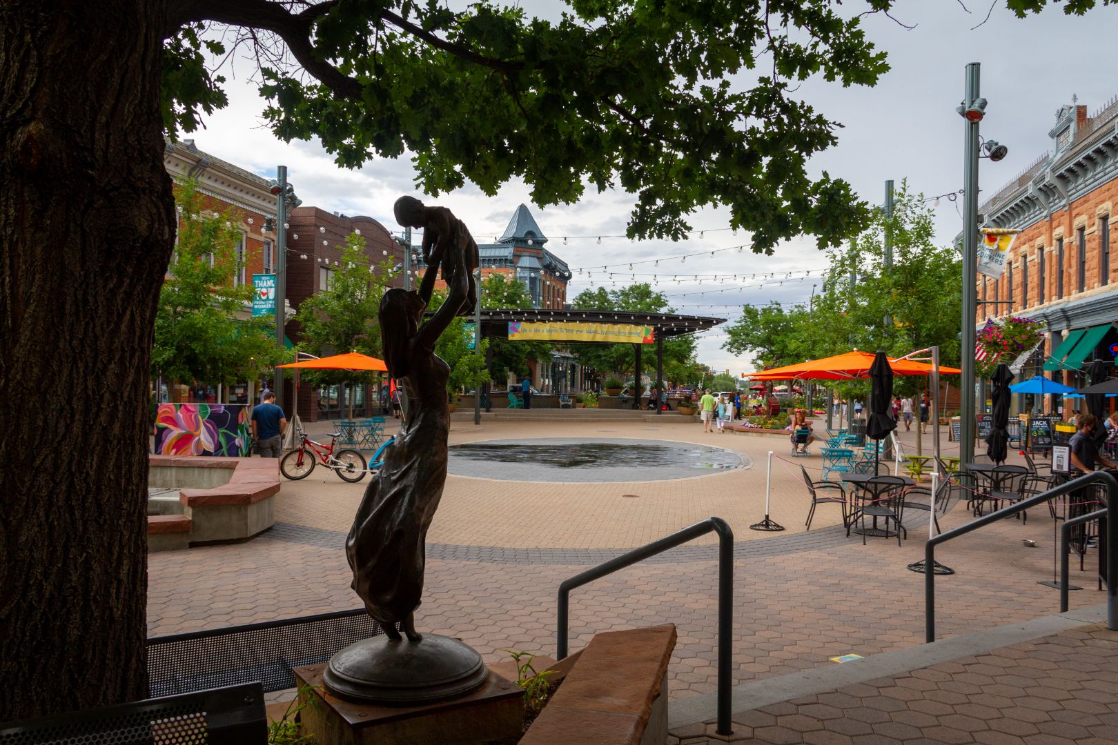 A beautiful day in downtown Fort Collins, Colorado. There are art installations, water features, and historic buildings.