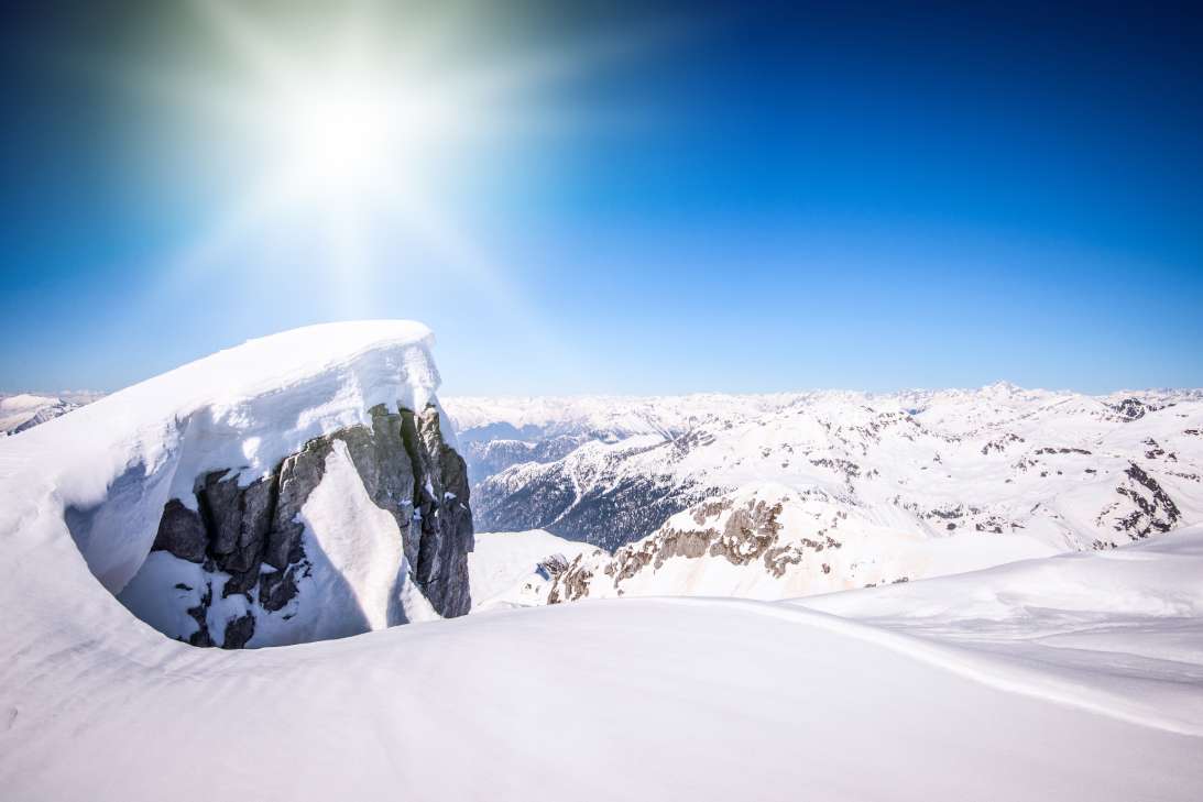 The dazzlingly bright sun shining down on a vast mountain range covered in a heavy, pristine blanket of snow.