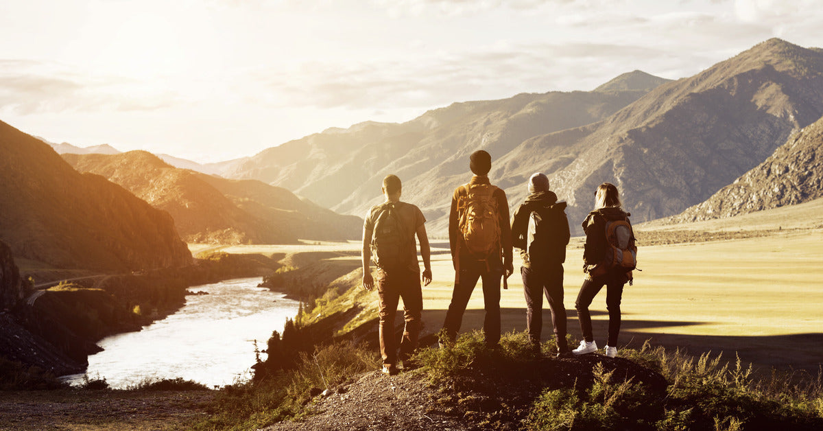 Four hikers standing on a hill looking at the surrounding mountain view. The sun is setting, basking everything in golden light.