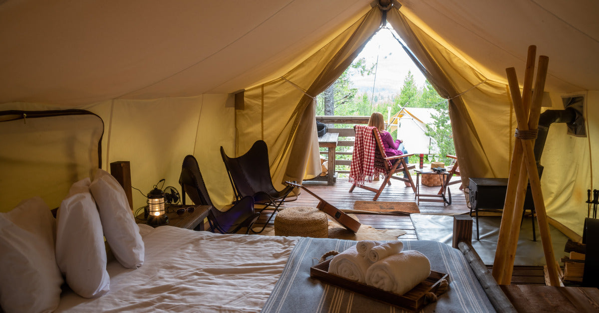 A woman sitting in the opening of a large tent set on a wooden platform. The tent is full of comfortable furniture.