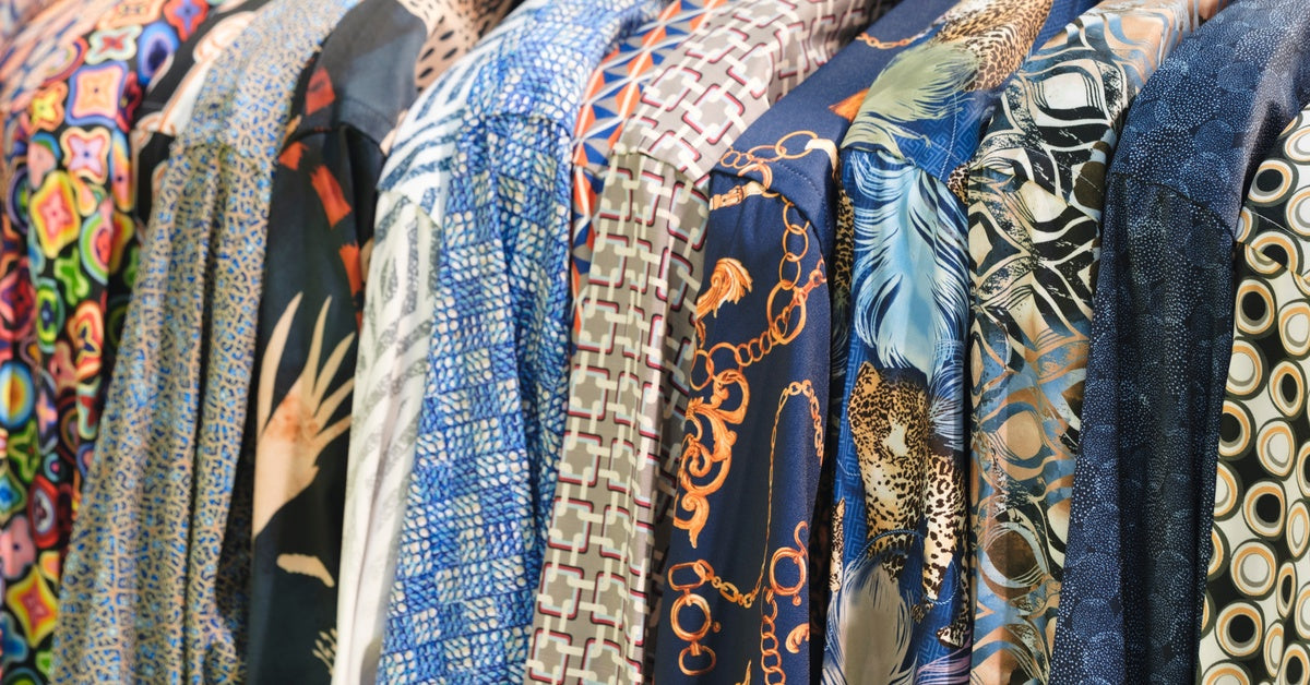 A row of men's shirts hanging together on a rack. They all have different colors and different bold prints.