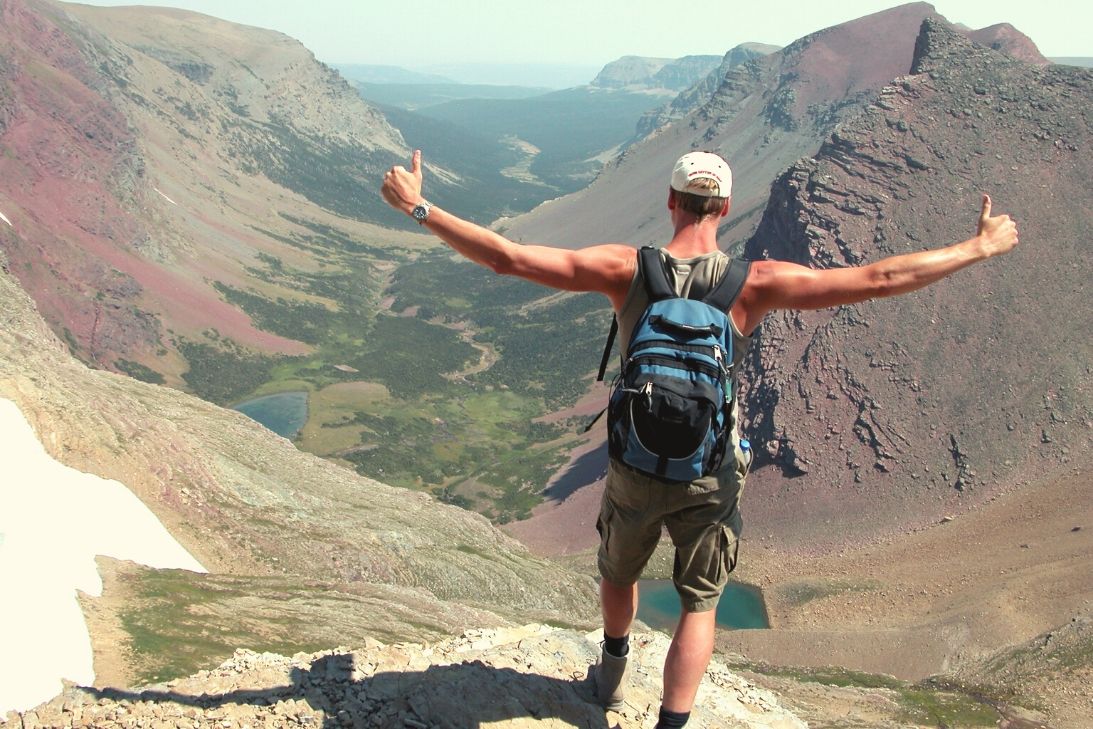 A man standing in a victorious pose in a mountain range.